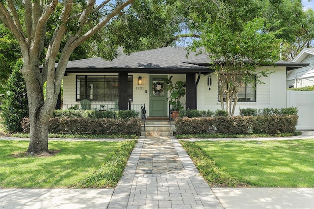 view of front of home featuring a front yard, covered porch, and a shingled roof