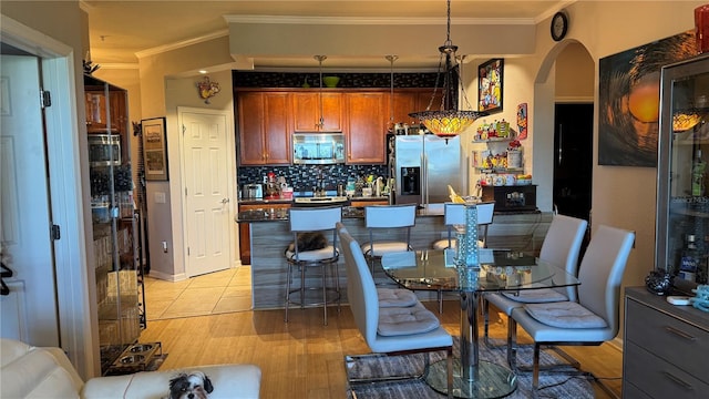 dining space featuring crown molding, arched walkways, bar with sink, and light wood-style floors