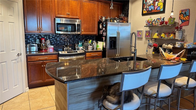 kitchen featuring stainless steel appliances, a sink, a kitchen breakfast bar, backsplash, and light tile patterned floors