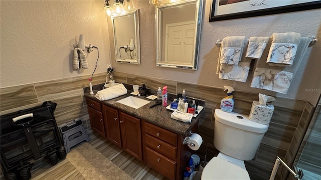 bathroom with a textured wall, vanity, toilet, and tile walls