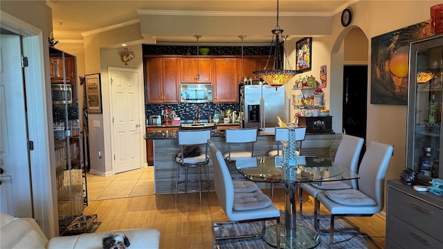 dining space featuring ornamental molding, arched walkways, and light wood-type flooring
