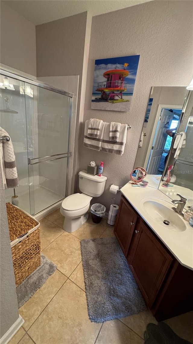 full bath with a shower stall, a textured wall, tile patterned flooring, toilet, and vanity