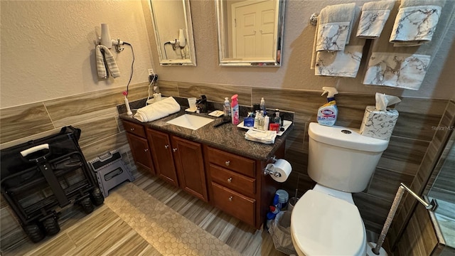 bathroom with a textured wall, toilet, vanity, and tile walls
