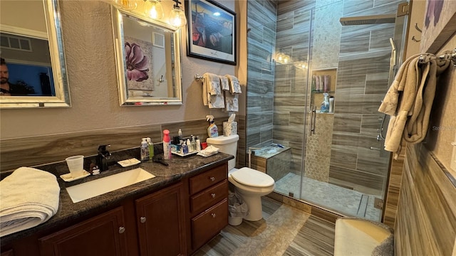 full bathroom featuring a textured wall, a stall shower, toilet, and vanity