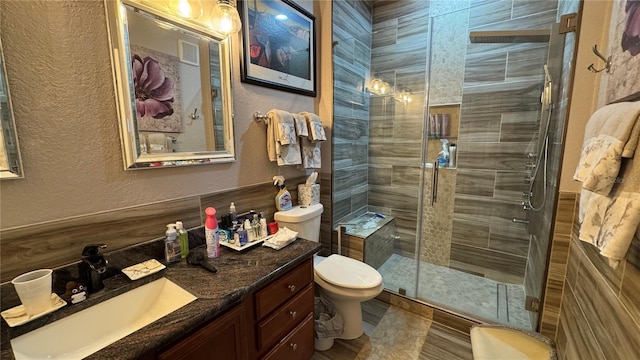bathroom with a textured wall, a shower stall, toilet, and vanity