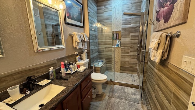 full bath featuring a textured wall, a shower stall, vanity, and toilet
