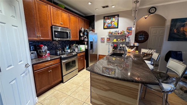 kitchen featuring stainless steel appliances, crown molding, a breakfast bar area, decorative backsplash, and a sink