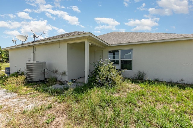 view of property exterior featuring central AC, stucco siding, and roof with shingles