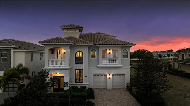 mediterranean / spanish house with a balcony, an attached garage, driveway, stucco siding, and a tiled roof
