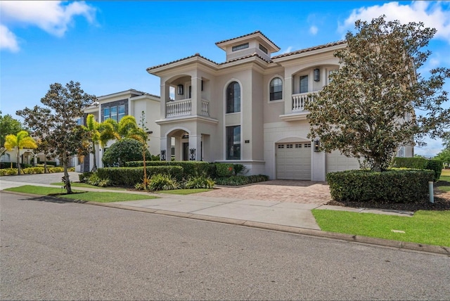 mediterranean / spanish-style house featuring a garage, a balcony, decorative driveway, stucco siding, and a tiled roof