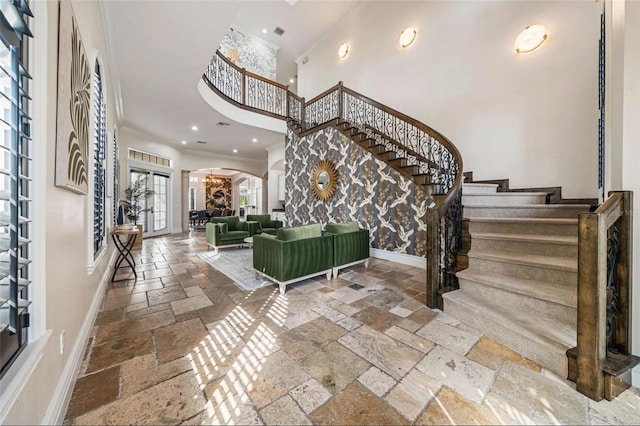 entryway with stone tile flooring, crown molding, stairs, arched walkways, and baseboards