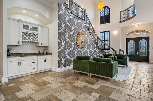 entrance foyer with stone tile flooring, a high ceiling, crown molding, bar area, and baseboards