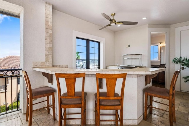 kitchen featuring tile countertops, plenty of natural light, stone tile flooring, ceiling fan, and recessed lighting