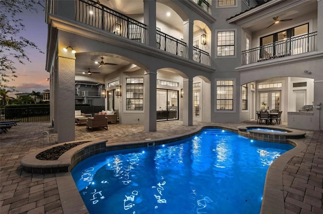 pool at dusk with a patio, french doors, an outdoor hangout area, a ceiling fan, and a pool with connected hot tub