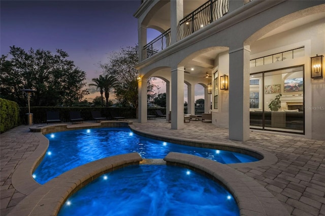 pool at dusk featuring a patio and a pool with connected hot tub