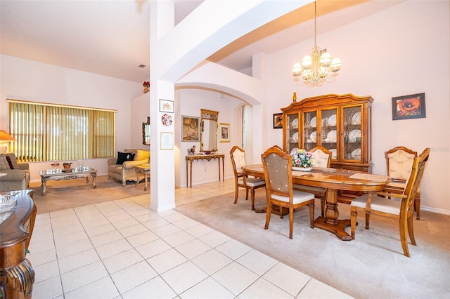 dining room featuring light carpet, arched walkways, a chandelier, a towering ceiling, and light tile patterned flooring
