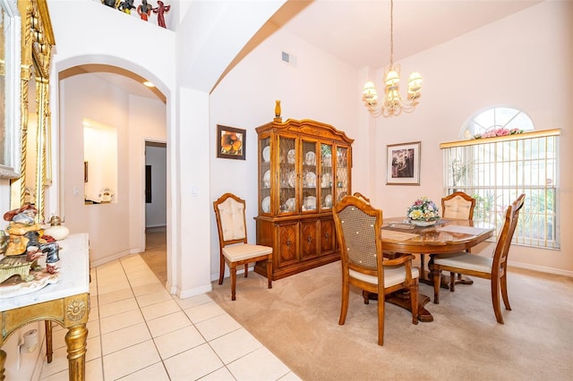 dining space featuring arched walkways, a high ceiling, light colored carpet, a chandelier, and baseboards