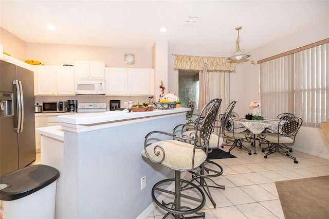 kitchen with appliances with stainless steel finishes, white cabinetry, light countertops, light tile patterned floors, and decorative light fixtures