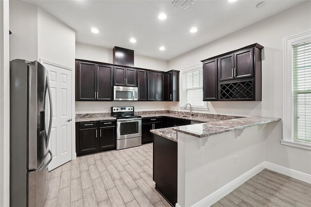 kitchen featuring stainless steel appliances, a peninsula, light wood finished floors, a sink, and plenty of natural light
