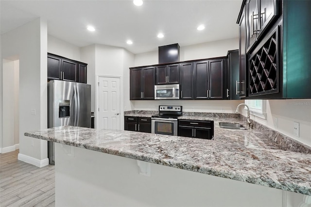 kitchen featuring appliances with stainless steel finishes, a sink, a peninsula, light stone countertops, and baseboards