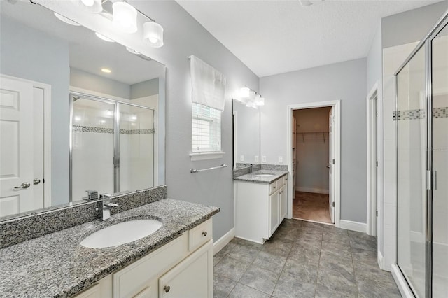 full bath with a shower stall, baseboards, a walk in closet, and two vanities