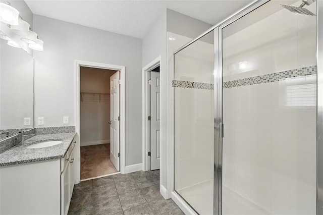 bathroom with a stall shower, vanity, a spacious closet, and baseboards