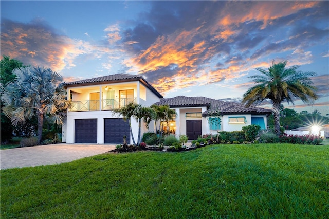 mediterranean / spanish home with a balcony, a lawn, stucco siding, an attached garage, and decorative driveway