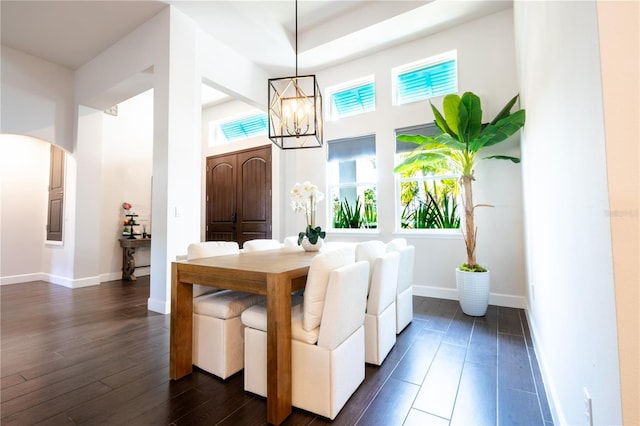 dining space featuring arched walkways, a chandelier, dark wood-style floors, a high ceiling, and plenty of natural light