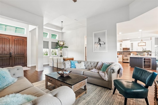 living room featuring light wood-style floors, beverage cooler, a tray ceiling, recessed lighting, and a chandelier