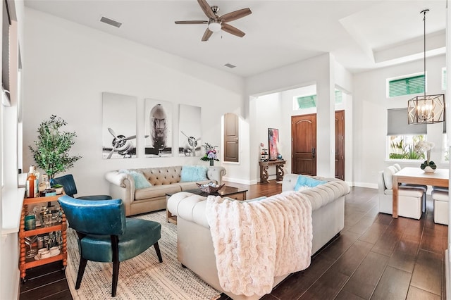 living area featuring a chandelier, dark wood finished floors, a ceiling fan, and baseboards