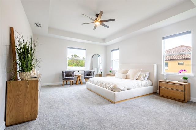 carpeted bedroom featuring a raised ceiling, baseboards, and a ceiling fan
