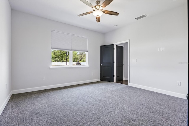 spare room featuring ceiling fan, dark colored carpet, and baseboards