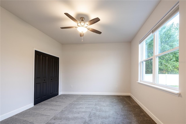 unfurnished bedroom featuring baseboards, dark colored carpet, a closet, and ceiling fan