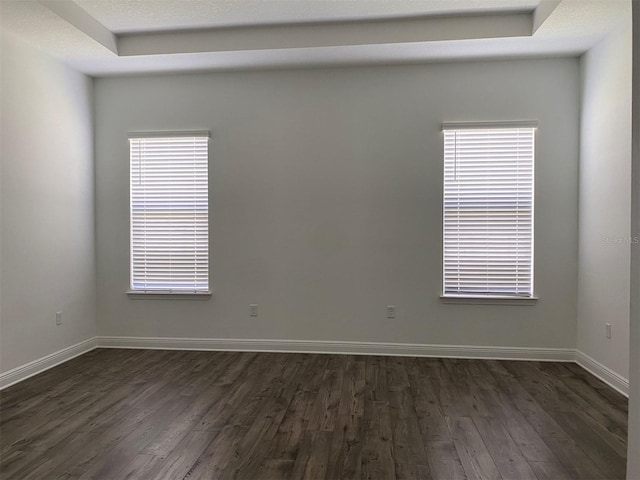 unfurnished room featuring dark wood-style floors, baseboards, and a raised ceiling