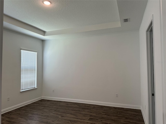 empty room featuring dark wood-style floors, a raised ceiling, baseboards, and a textured ceiling
