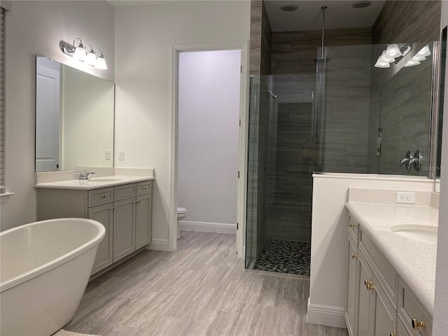 bathroom featuring a stall shower, two vanities, toilet, baseboards, and a freestanding tub