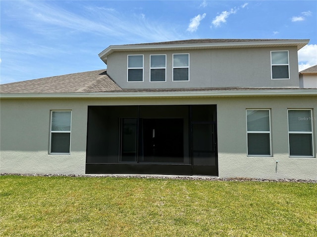 back of property with a sunroom, stucco siding, and a yard