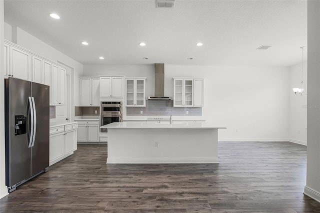 15161 Lake Bessie Loop, Winter Garden, FL 34787 - kitchen featuring appliances with stainless steel finishes, wall chimney range hood, tasteful backsplash, white cabinets, and a kitchen island with sink