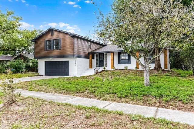 7085 Willowwood St, Orlando, FL 32818 - tri-level home featuring a garage, concrete driveway, a front yard, and brick siding