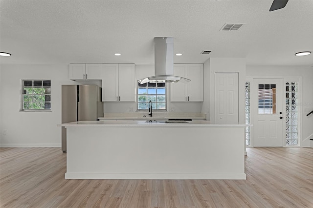 7085 Willowwood St, Orlando, FL 32818 - kitchen featuring island exhaust hood, light countertops, light wood finished floors, a center island, and freestanding refrigerator