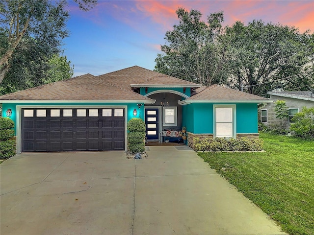 view of front of home featuring a front lawn, stucco siding, an attached garage, stone siding, and driveway