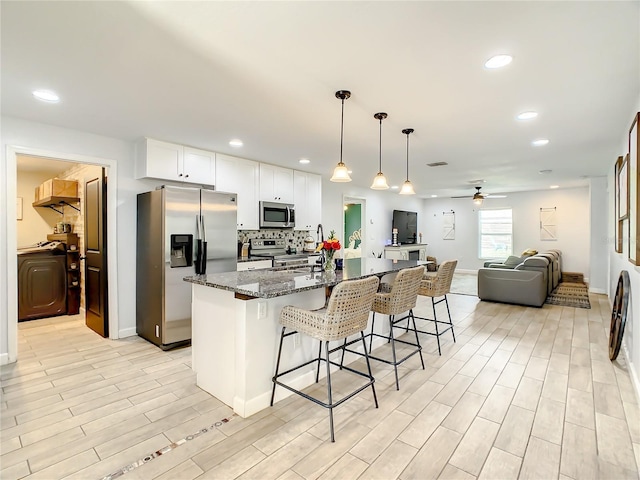 kitchen featuring appliances with stainless steel finishes, a ceiling fan, a breakfast bar area, dark stone counters, and white cabinetry