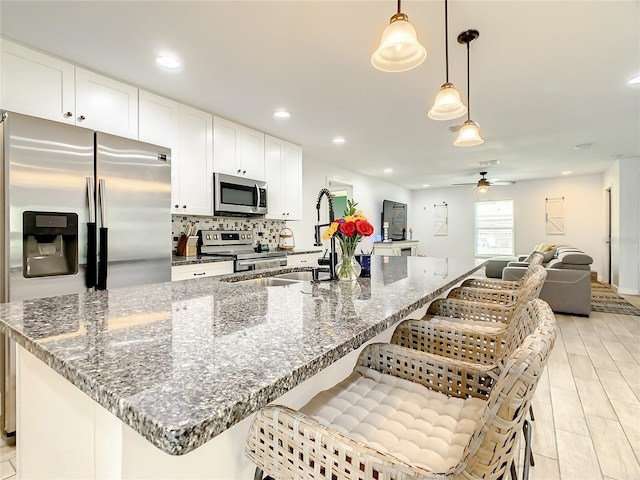 kitchen featuring stainless steel appliances, a ceiling fan, a sink, decorative backsplash, and white cabinetry