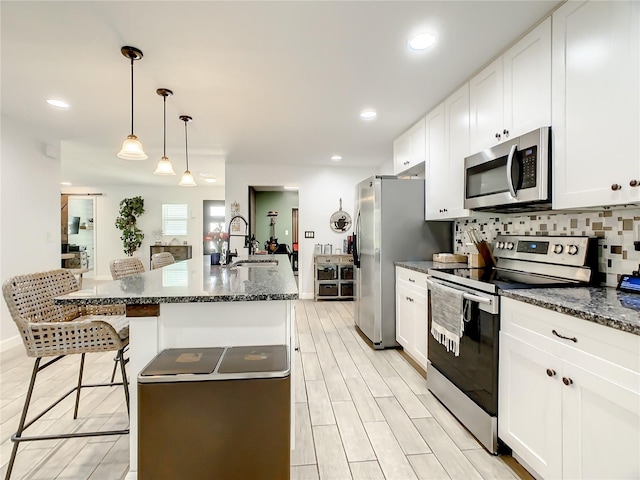 kitchen featuring stainless steel appliances, a sink, a breakfast bar area, white cabinetry, and a kitchen island with sink