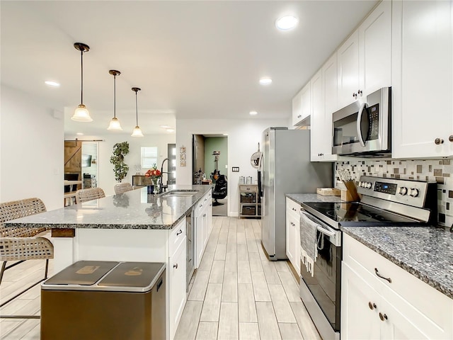 kitchen with appliances with stainless steel finishes, a sink, an island with sink, white cabinetry, and recessed lighting
