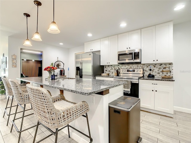 kitchen with stainless steel appliances, backsplash, white cabinetry, a center island with sink, and recessed lighting