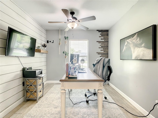 home office with ceiling fan, baseboards, light wood-type flooring, and wooden walls