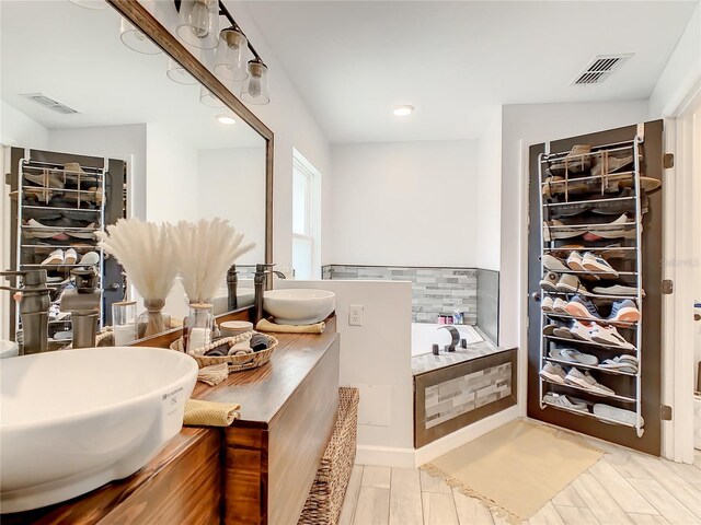 bathroom featuring a bath, a walk in closet, double vanity, recessed lighting, and tasteful backsplash