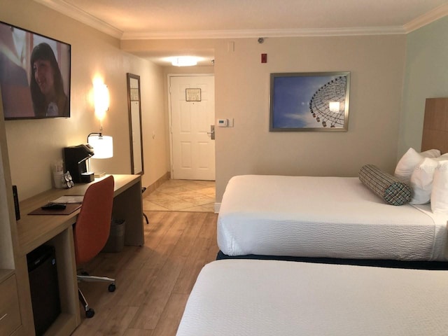 bedroom featuring ornamental molding, light wood-style flooring, and a desk