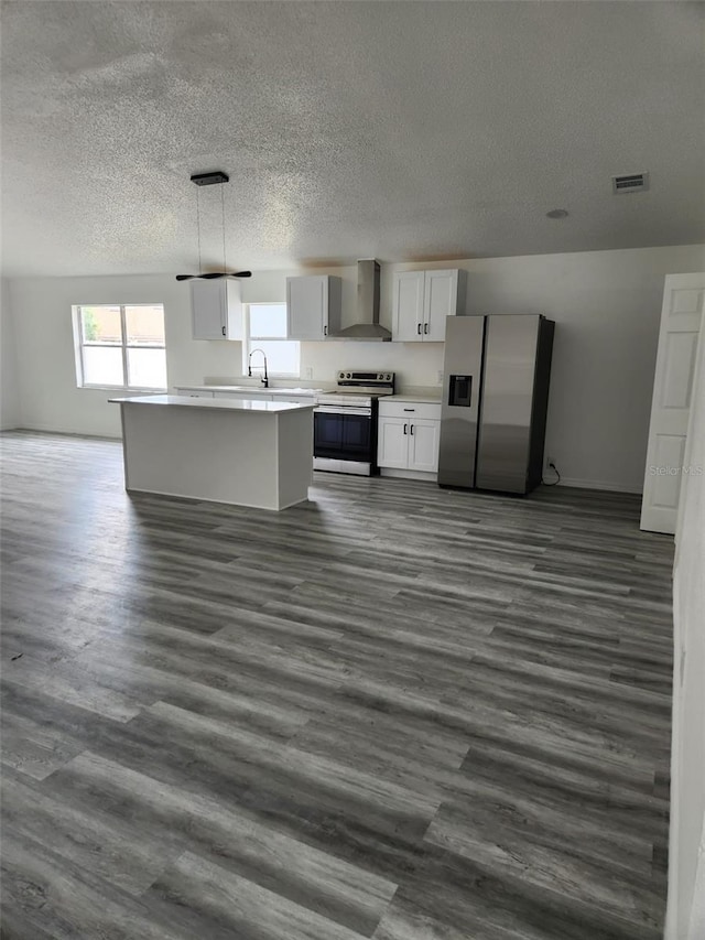 kitchen featuring appliances with stainless steel finishes, wall chimney range hood, a textured ceiling, light countertops, and white cabinetry